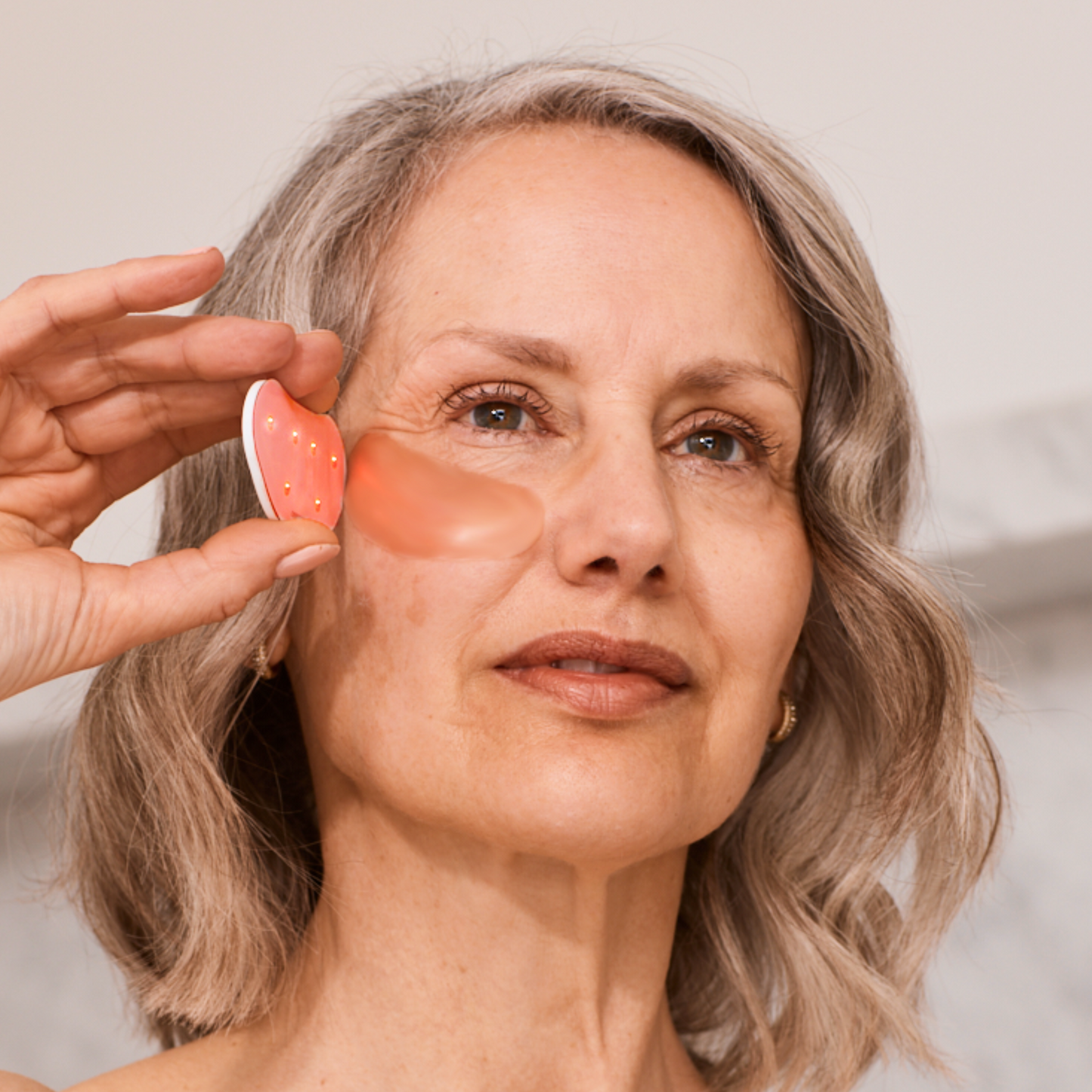 Older woman using omnilux infrared device on undereye area with patch on skin