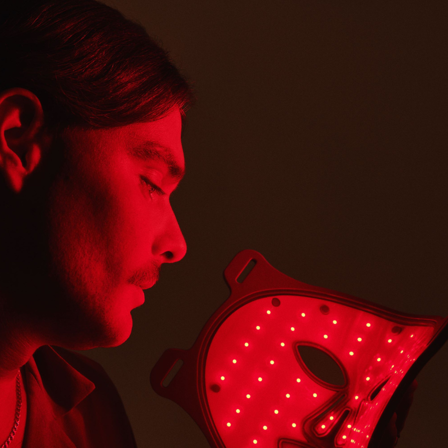 Man holding omnilux men's red light therapy mask in from of him with lights on